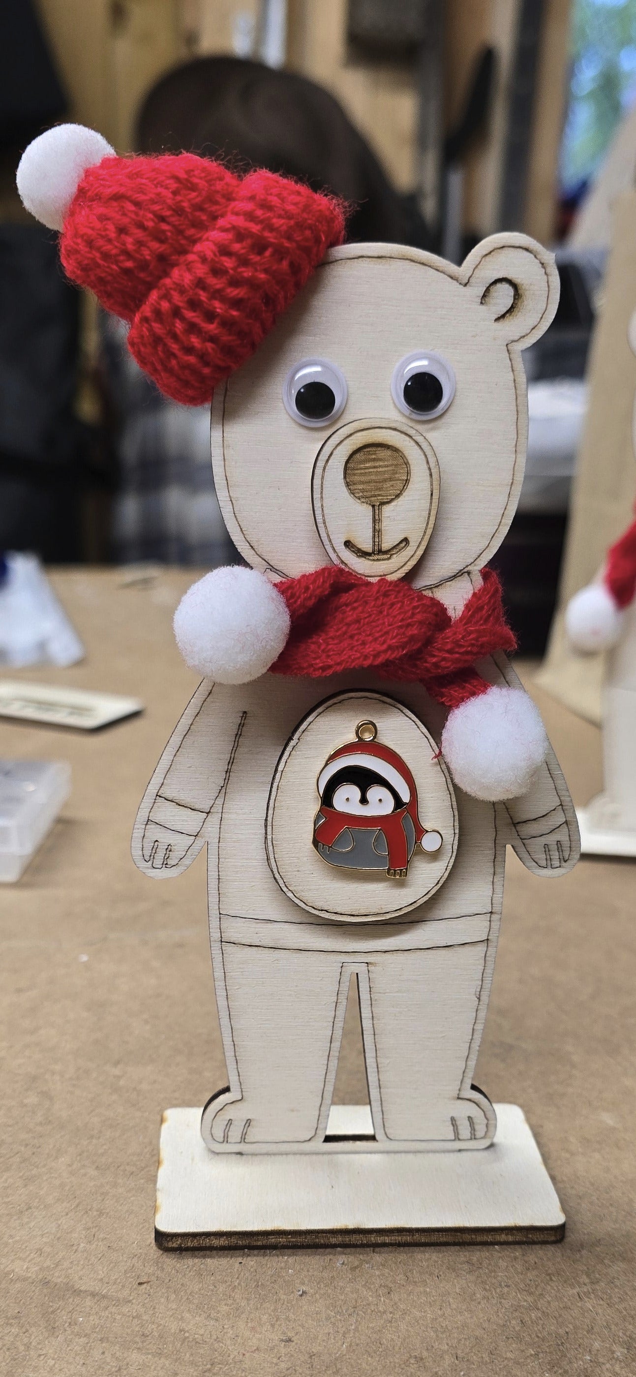 Wooden bear figurine with a red scarf and white pom-pom on a brown surface.